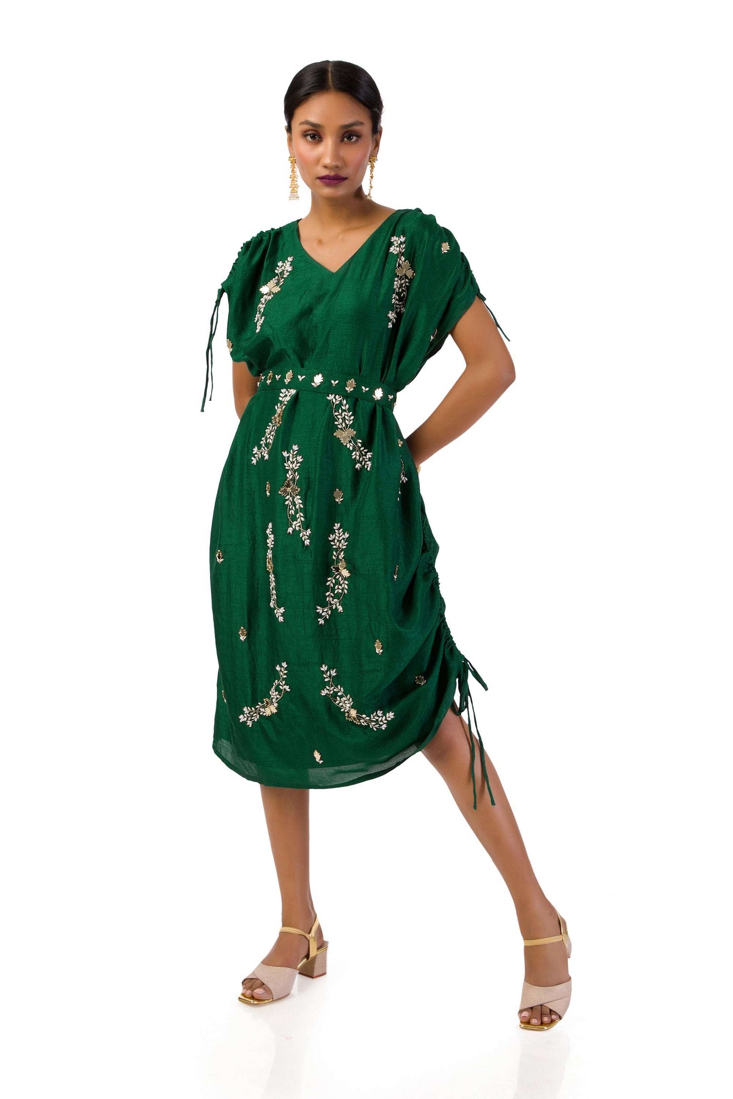 Woman wearing a bottle green one-shoulder draped gown in semi-silk with hand embroidery, paired with a matching belt.