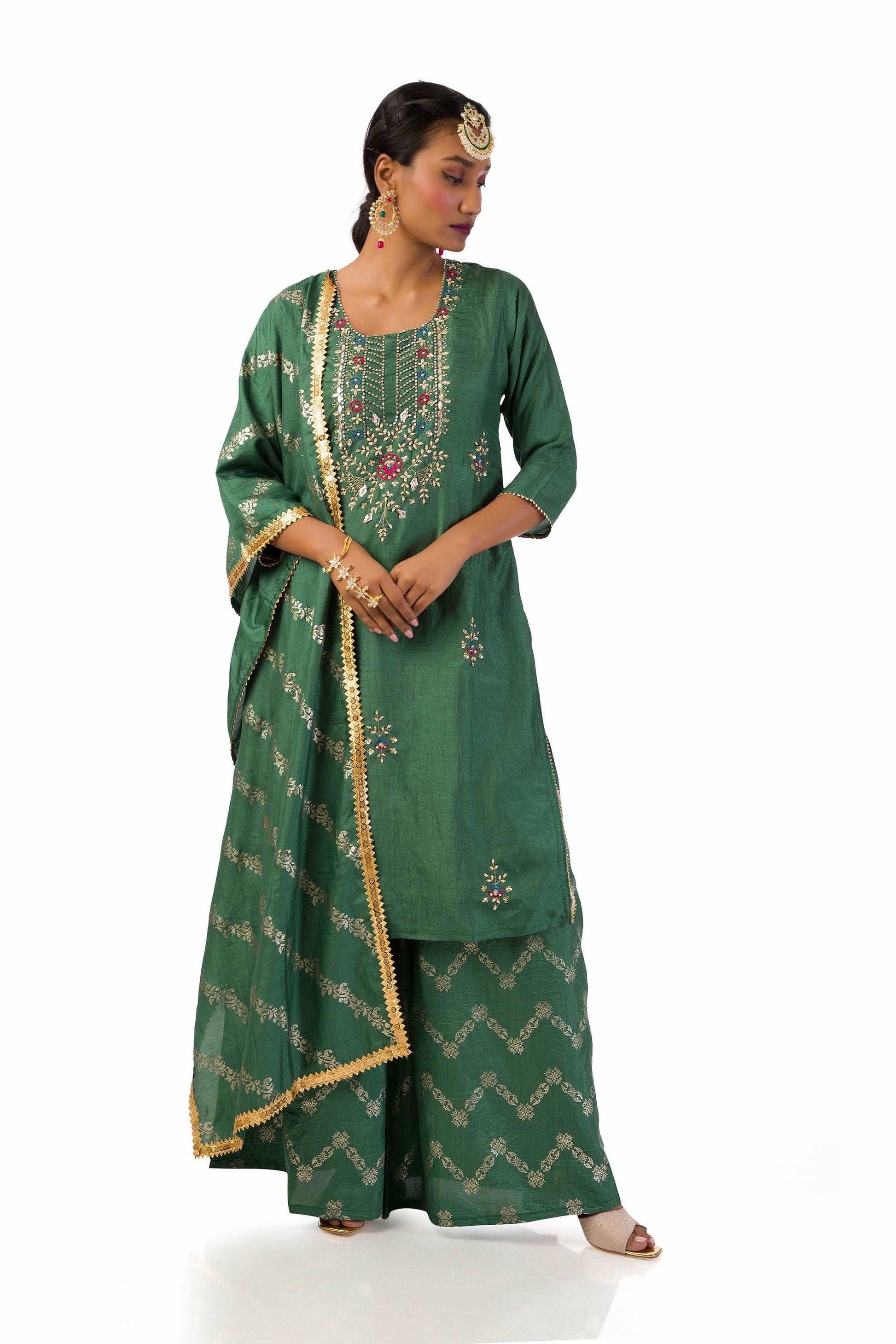 Woman wearing a dust green semi-silk kurta set with hand embroidery and print, paired with matching palazzo pants and dupatta.