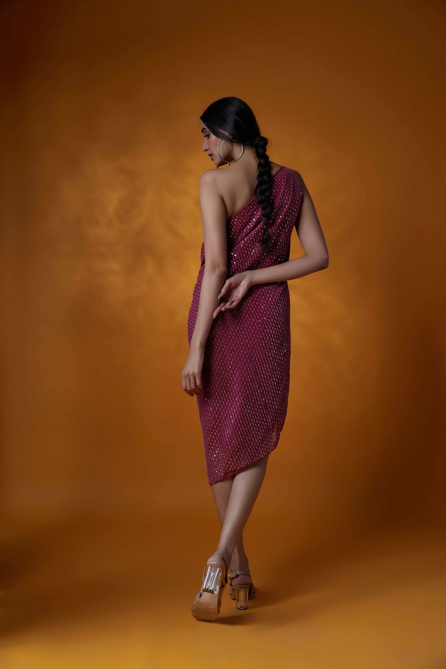 Model wearing a pink sequin one-shoulder dress against an orange background