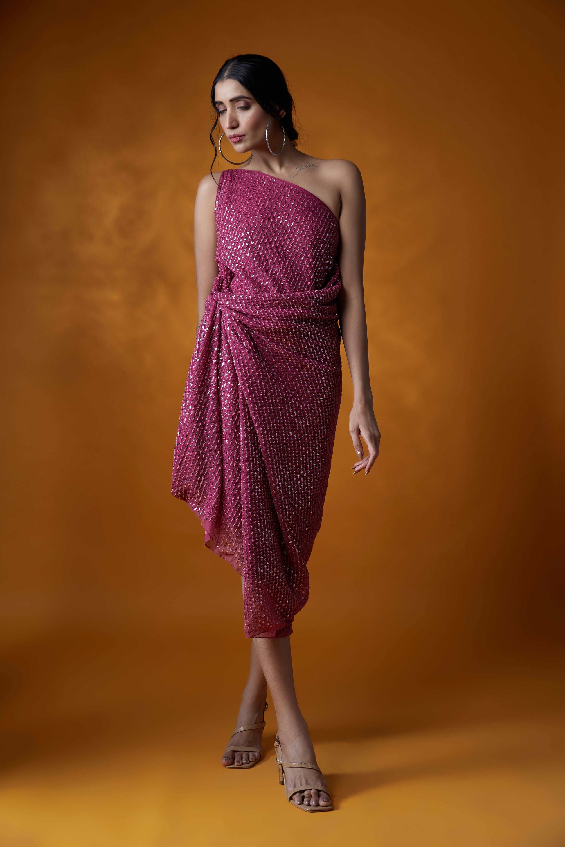 Model wearing a pink sequin one-shoulder dress against an orange background